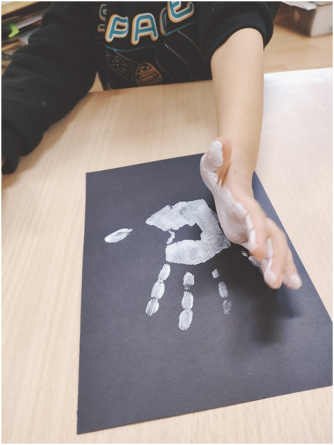 huella de manos de niño en pintura blanca sobre cartulina negra