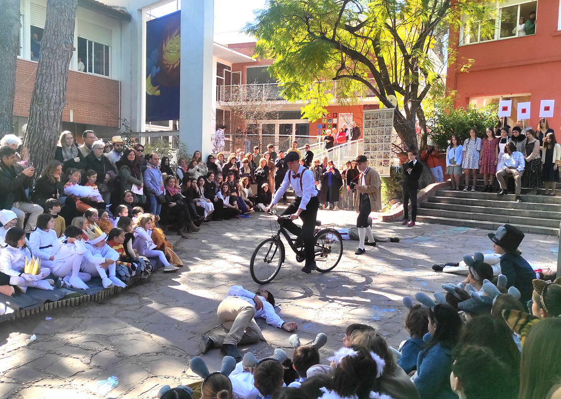 Un joven disfrazado de los años 20 pasea en bicicleta por el jardín del Centro Educativo Gençana, mientras otros compañeros yacen en el suelo tumbados. Interpretación de "Las bicicletas son para el verano" de los alumnos de 4º ESO en el Desfile del XXXV Carnaval Literario