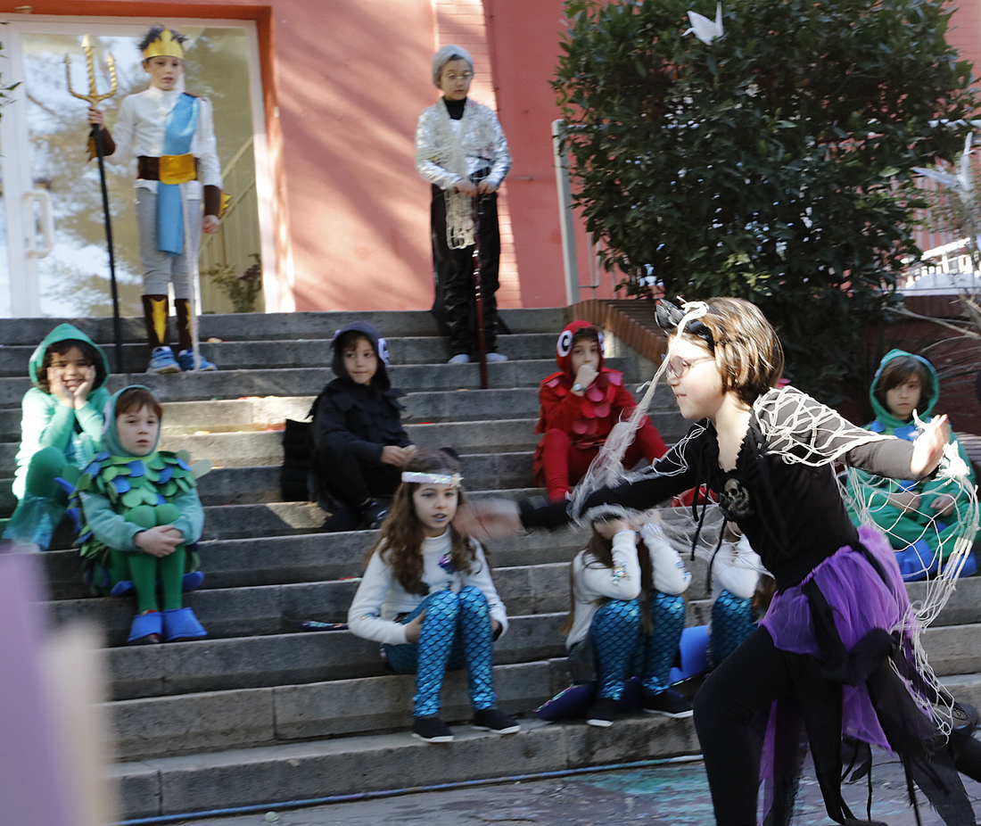 Una niña disfrazada de araña corre por el jardín del Centro Educativo Gençana mientras otros compañeros la miran sentados en las escaleras. Interpretación de 3º Educación Primaria durante el Desfile del XXXV Carnaval Literario