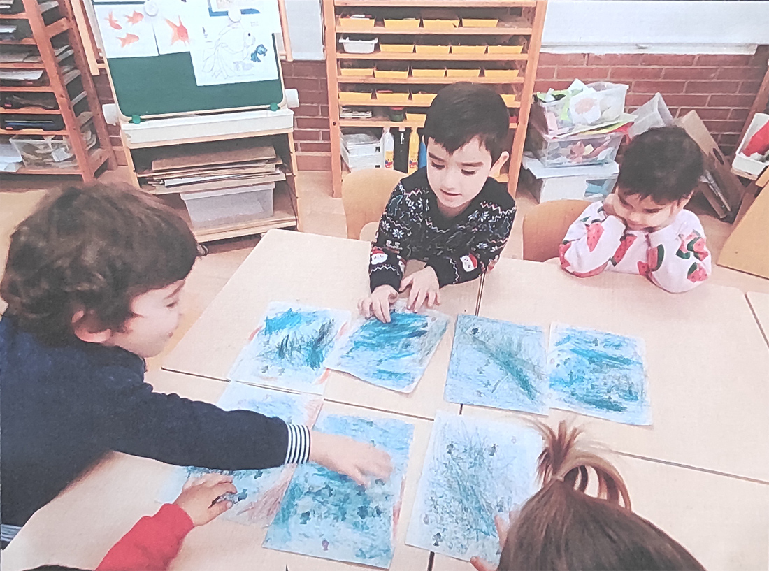 Cuatro niños de 3 años están pintando en color azul encima de su mesa del colegio