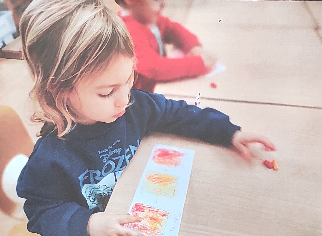 Una niña rubia, que aparece de perfil, pinta de colores rojos en un papel