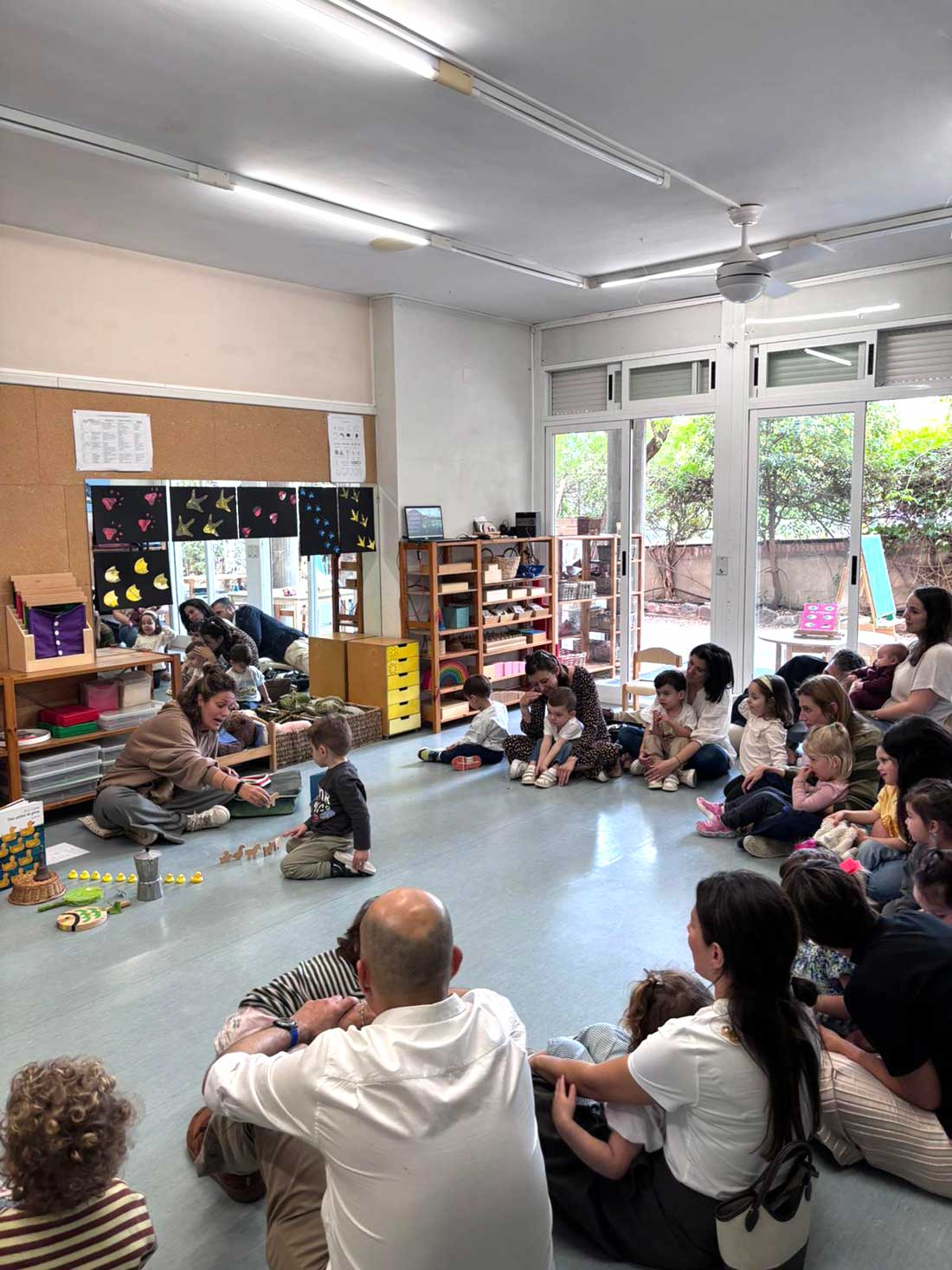 Una maestra de Gençana cuenta un cuento a las familias de la clase de 2 años mientras ellas lo escuchan junto a sus hijos en un corro alrededor